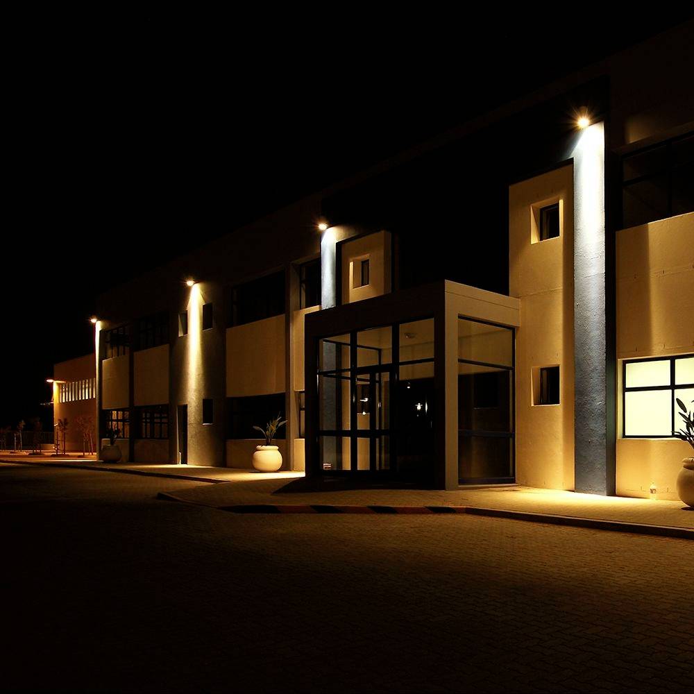 Een modern gebouw is 's nachts verlicht. Rechthoekige ramen en een vooringang zijn zichtbaar. Straatlampen verlichten de omgeving.