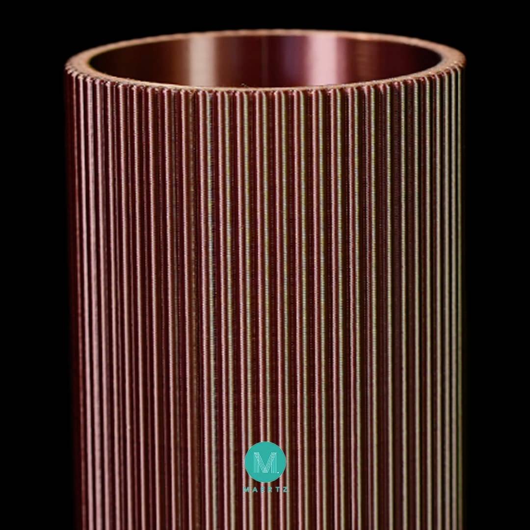 Een cilindrisch metalen voorwerp met verticale groeven en een metallische glans tegen een zwarte achtergrond. Onderaan bevindt zich een blauw logo.