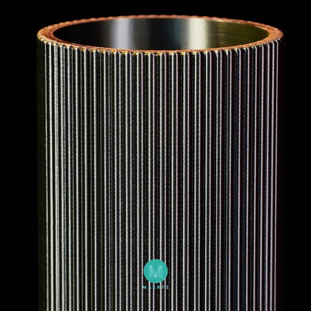 'MMMS'-logo op een zwarte achtergrond met een cilindrisch metalen object met verticale groeven en een oranje-gouden rand bovenaan.