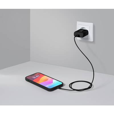 Een smartphone ligt op een tafel en wordt via een kabel opgeladen aan een oplader die is aangesloten op een stopcontact in de muur.