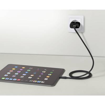 Een tablet ligt op een tafel en is aangesloten op een stopcontact met een kabel. Het scherm toont talrijke kleurrijke app-symbolen.