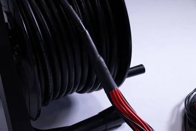 Een grote kabelspoel met zwart kabel opgerold en rode draden zichtbaar op de voorgrond tegen een lichte achtergrond.
