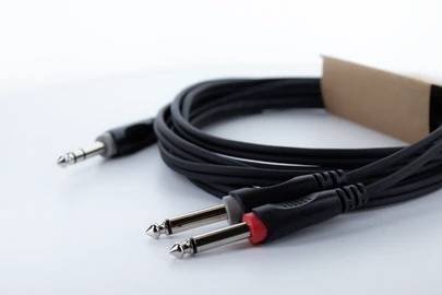 Een zwarte audiokabel met meerdere jackstekkers, gedeeltelijk verzegeld, ligt los opgerold op een witte achtergrond.