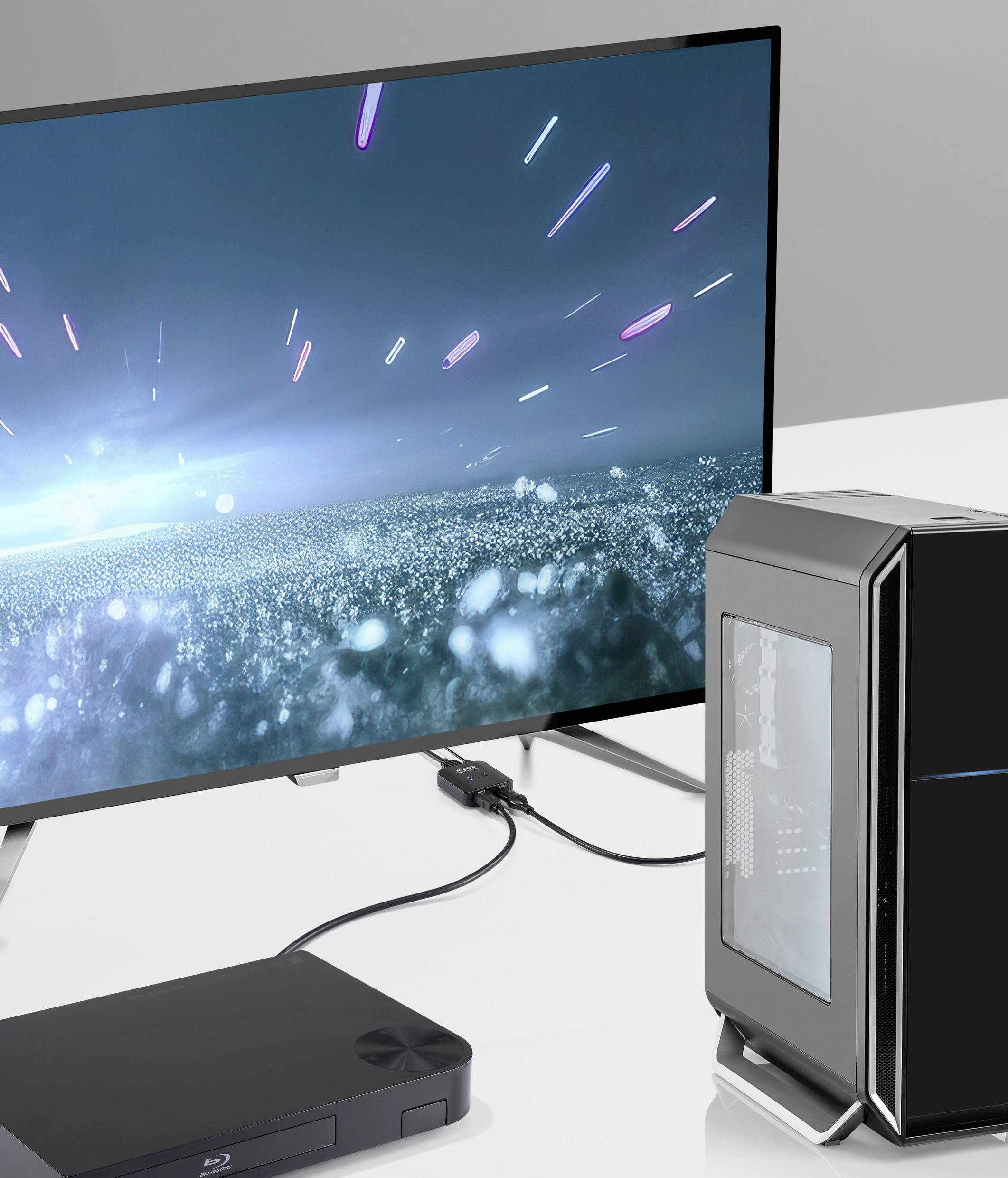 Een glanzende computer, een gameconsole en een groot scherm met futuristische graphics die de technologie in de moderne woonkamer laten zien.