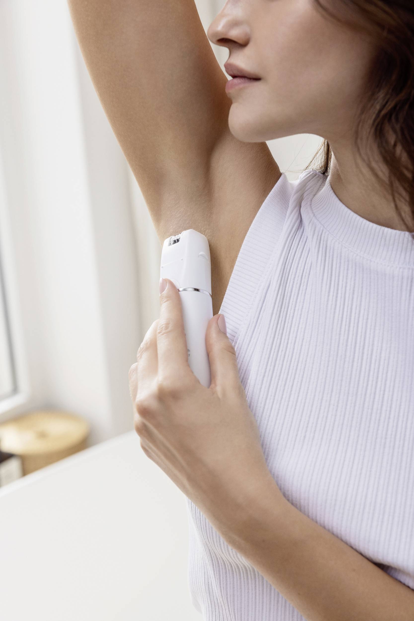 Een vrouw brengt deodorant aan op haar oksel. Ze draagt een wit bovenkleding en bevindt zich in een lichte ruimte.