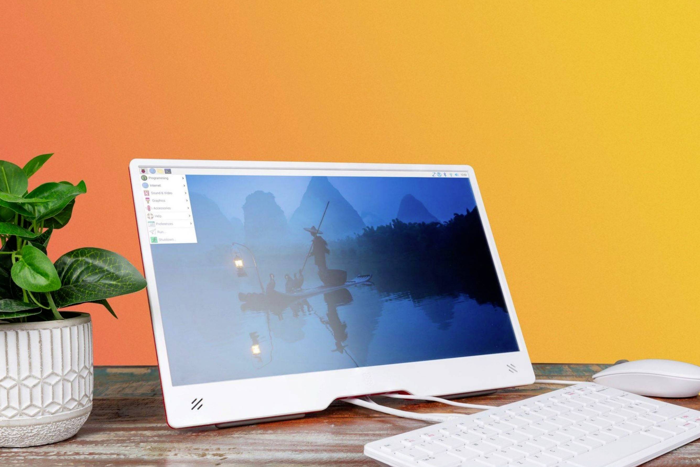 Een moderne desktopcomputer op een tafel, naast een plant. Het scherm toont een afbeelding met boten op rustig water.