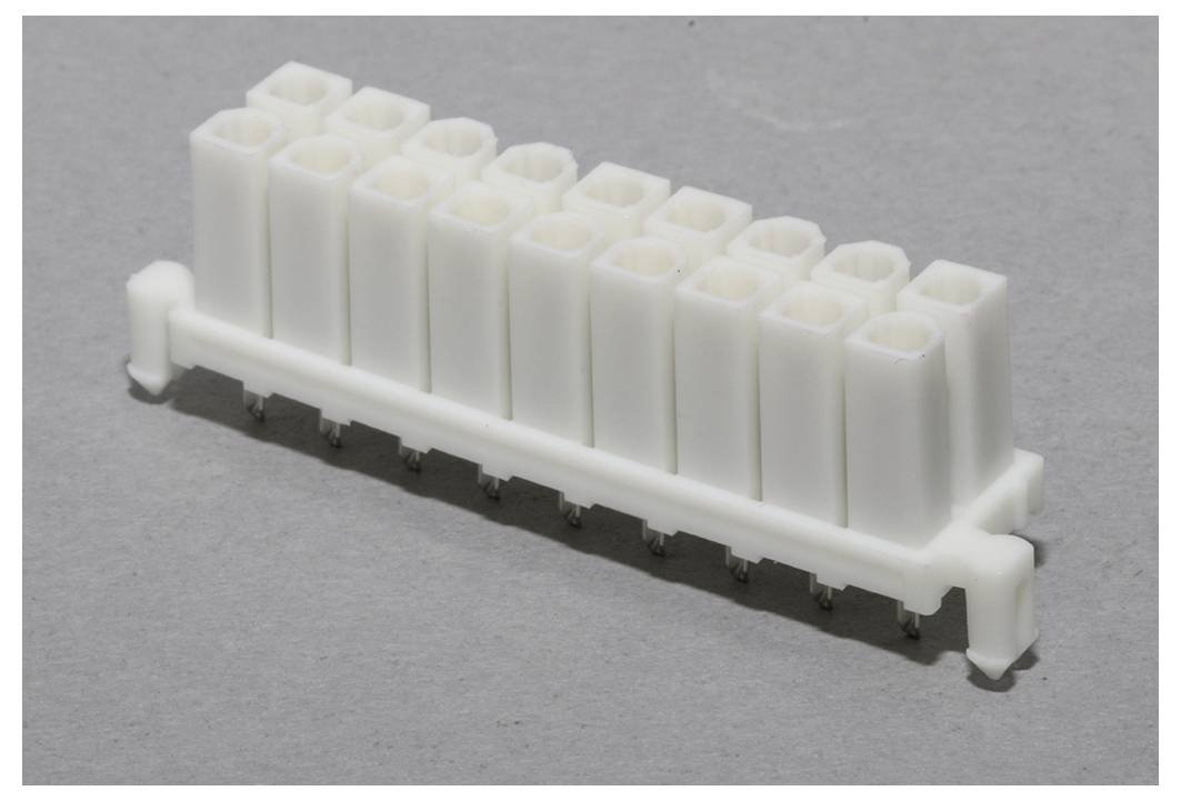 Witte stekkerstrip met meerdere aansluitingen op grijze achtergrond, toont een rij elektrische aansluitklemmen.