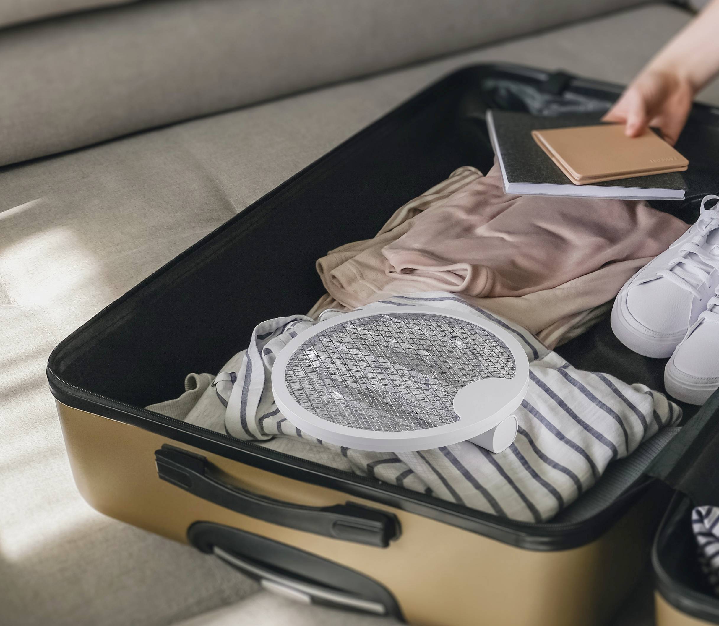 Een opengevallen koffer met kledingstukken, notitieboeken en een paar sneakers, klaar om in te pakken voor een reis.