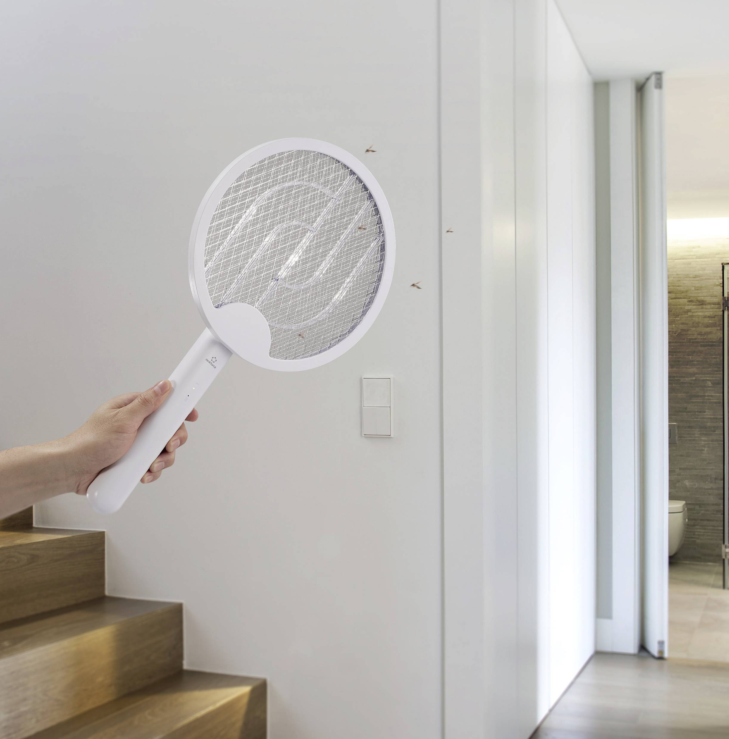 Een persoon houdt een elektrische vliegenmepper vast in de gang om drie vliegen aan de muur te verjagen.