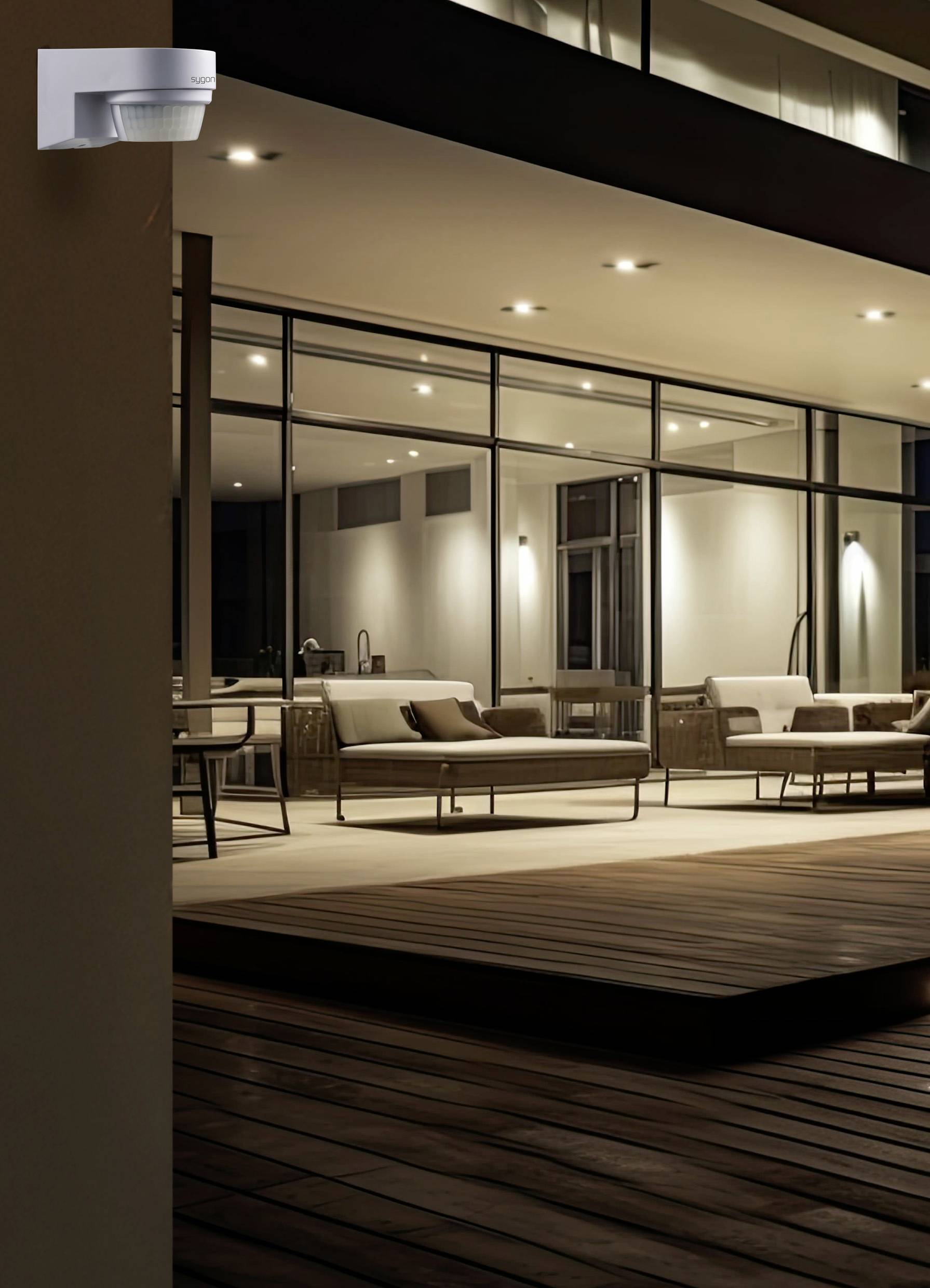 Een moderne woonruimte met grote glasgevels en een stijlvol terras, verlicht bij het invallen van de avond, bank en zithoek op de voorgrond.