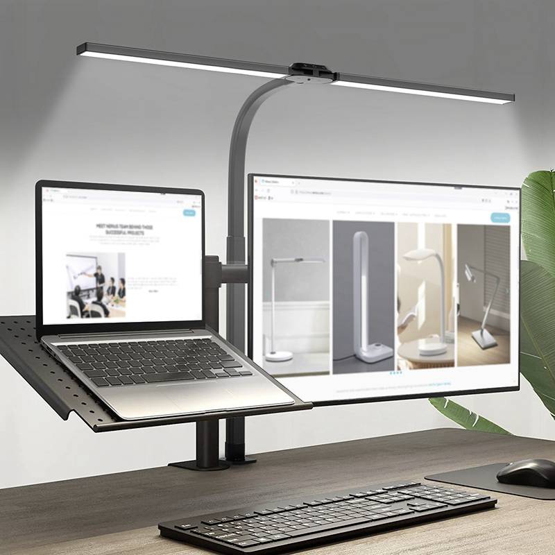 Een laptop op een tafel met een verstelbare lamp; ernaast staat een groot scherm met productafbeeldingen, omringd door planten.