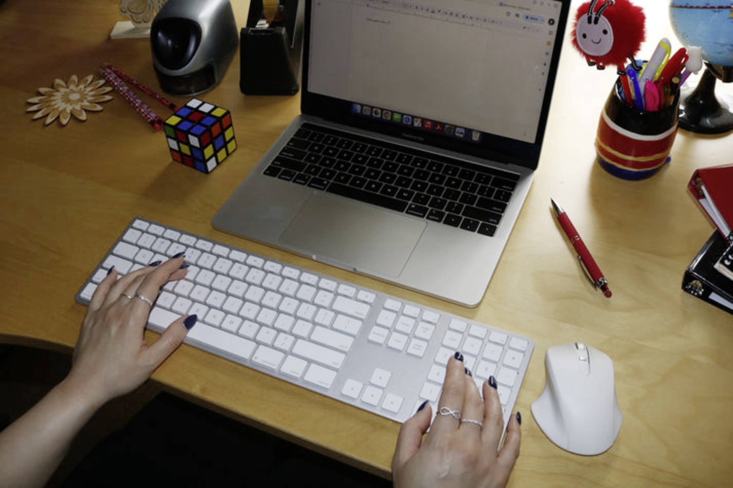 Een persoon typt op een extern toetsenbord voor een laptop op een bureau. Naast het toetsenbord liggen een Rubik's Cube en schrijfbenodigdheden.