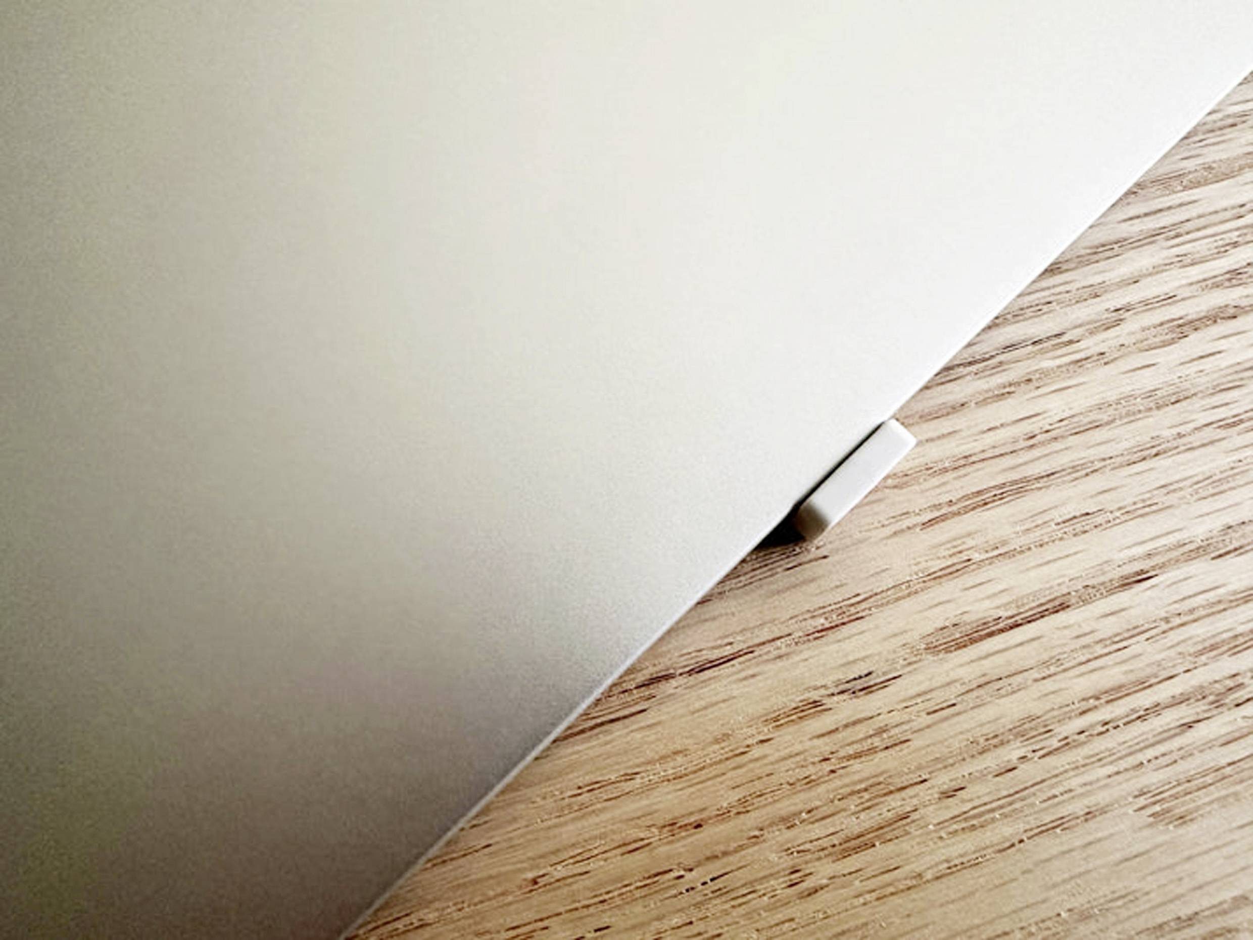 Een laptop, gedeeltelijk gesloten, ligt op een houten tafel. Een deel van de hoek steekt uit, zonder verdere zichtbare objecten.