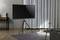 Woonkamer met moderne tv op een standaard, houten vloer, grijs tapijt, dressoir met boeken, tafel met vaas en gordijnen op de achtergrond.
