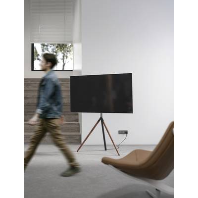 Moderne ruimte met een groot flatscreen-scherm op een standaard, een onscherpe persoon die langs loopt, lichte wanden, stoel op de voorgrond.