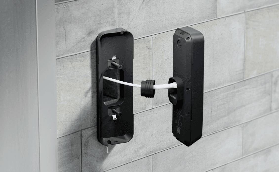 Zwart smart-slot wordt geïnstalleerd aan een grijze muur. Een kabel verbindt het binnendeel met de buitenkant van de deur.