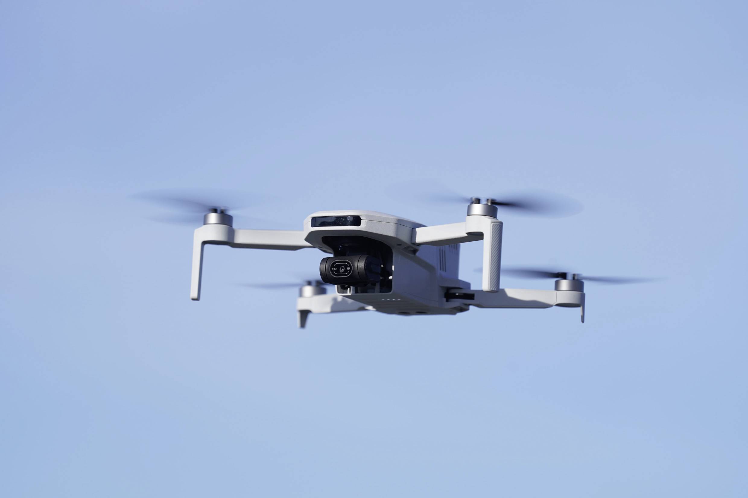 Een witte drone vliegt aan de heldere blauwe lucht, zijn rotorbladen draaien snel.