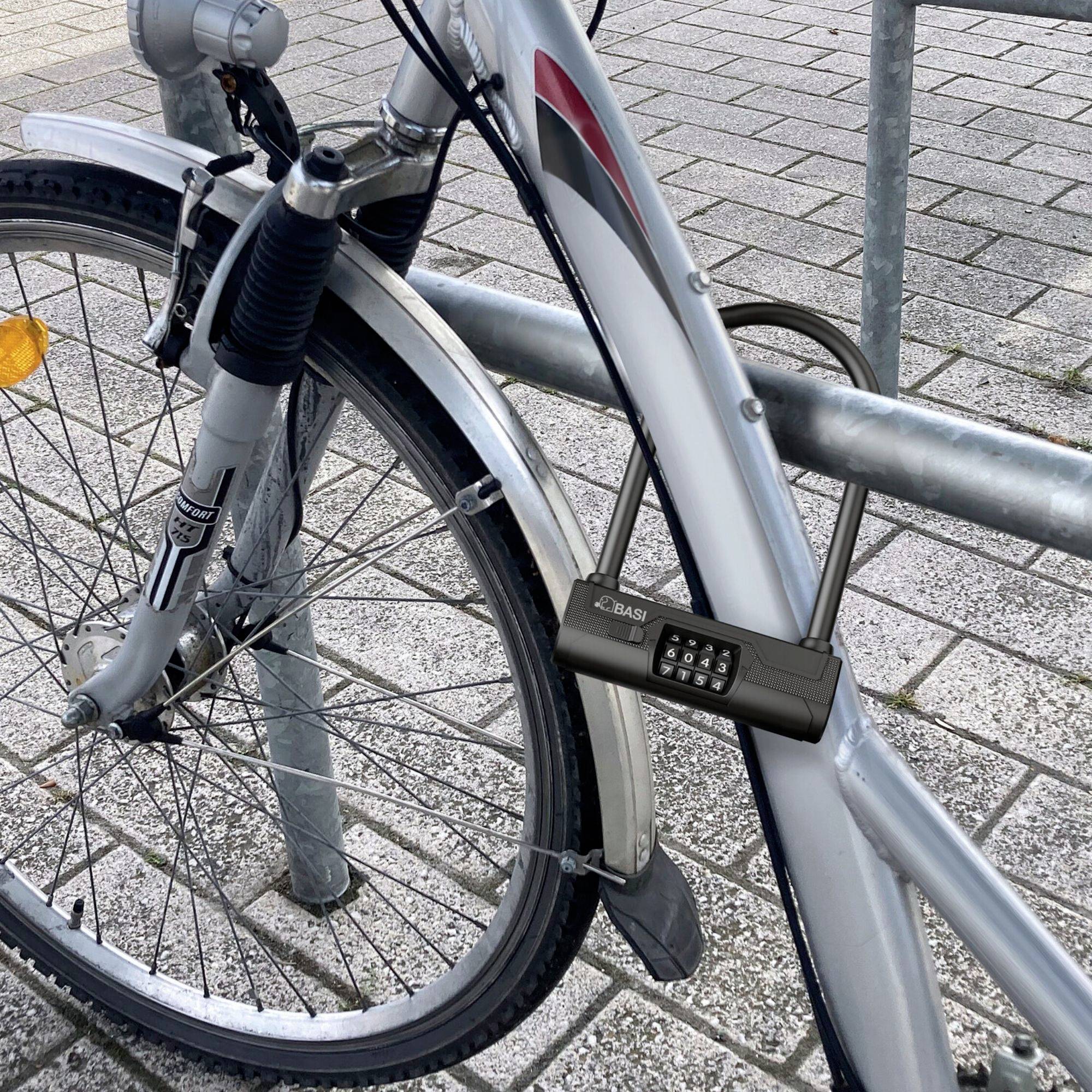 Een zilveren fiets met een zwart cijferslot, bevestigd aan een fietsenrek, staat op een geplaveid voetpad.