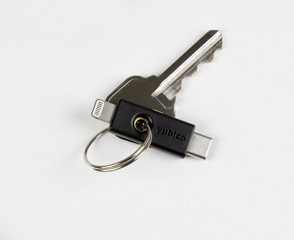 Een USB-C-beveiligingsstick en een sleutel aan een sleutelhanger liggen op een wit oppervlak.