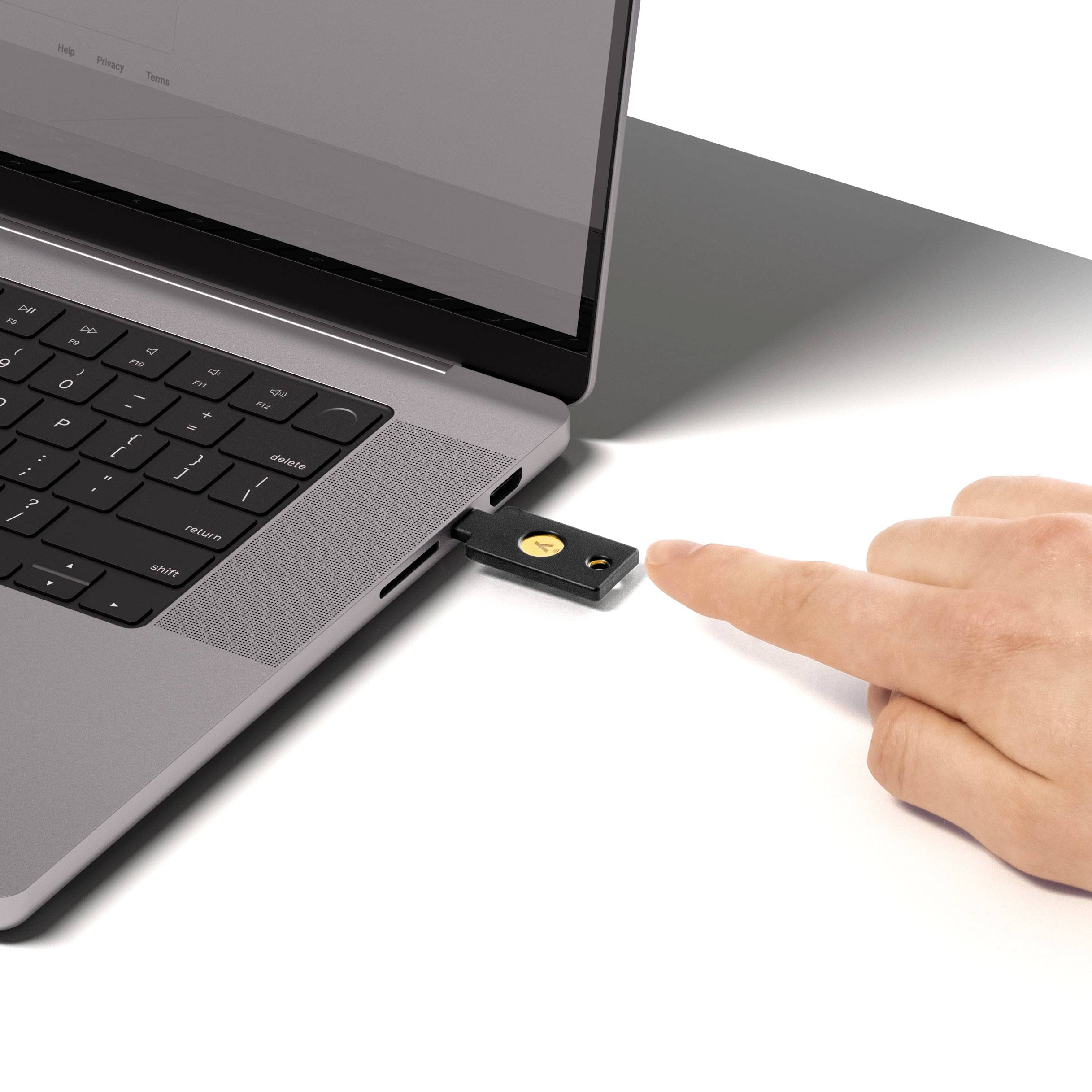 Een laptop met een geplaatste USB-beveiligingssleutel. Een hand wijst naar de sleutel, wat duidt op een beveiligingscontrole.