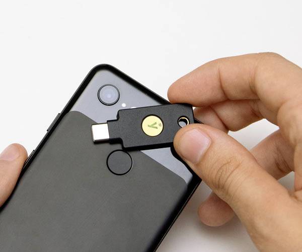 Een hand houdt een USB-beveiligingssleutel vast die in een smartphone wordt gestoken.