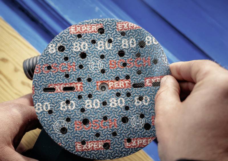 De 'Orbital-excentrische slijper' wordt gebruikt met schuurpapier van Bosch. Het papier toont korrelgrofte 80 en de 'Expert'-opdruk. Handen stellen het papier af.