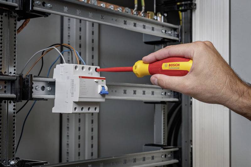 Een persoon draait een schroef vast met een schroevendraaier in een elektrische schakelkast. Kabels zijn aangesloten.