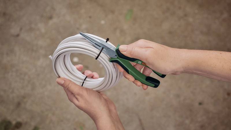 Een hand houdt een tang en knipt een wit snoer door dat door een andere hand wordt vastgehouden.