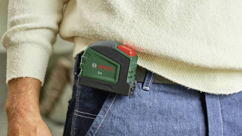 Persoon met een Bosch-meetlint bevestigd aan de spijkerbroek, klaar voor klussen.