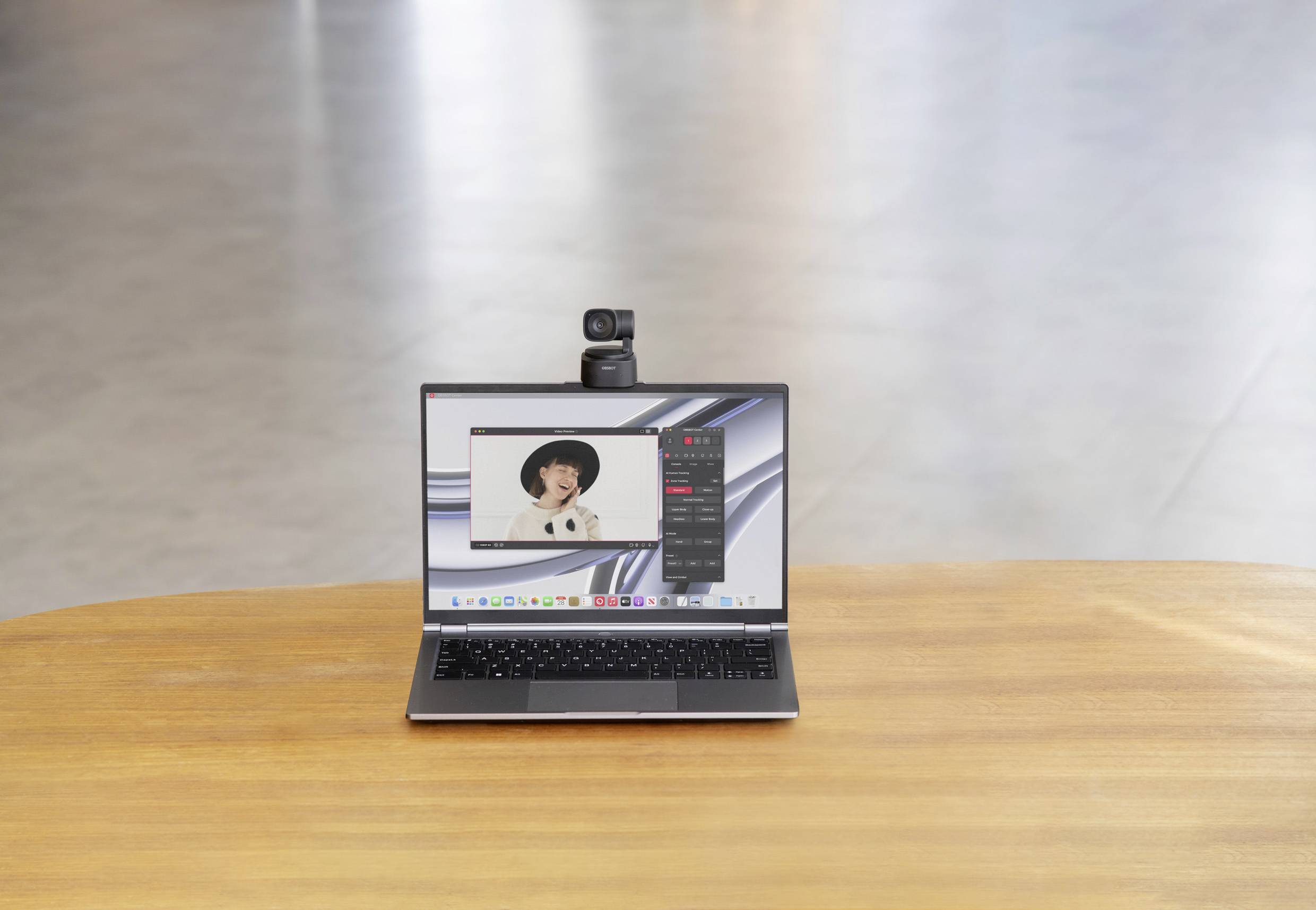 Een laptop op een houten tafel toont een videogesprek met een persoon die een hoed draagt. Een camera is bovenaan de laptop bevestigd.