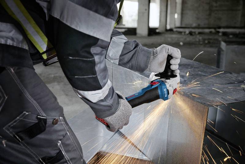 Een persoon snijdt metaal met een blauwe haakse slijper, vonken spatten rond. Hij draagt beschermende kleding en handschoenen.
