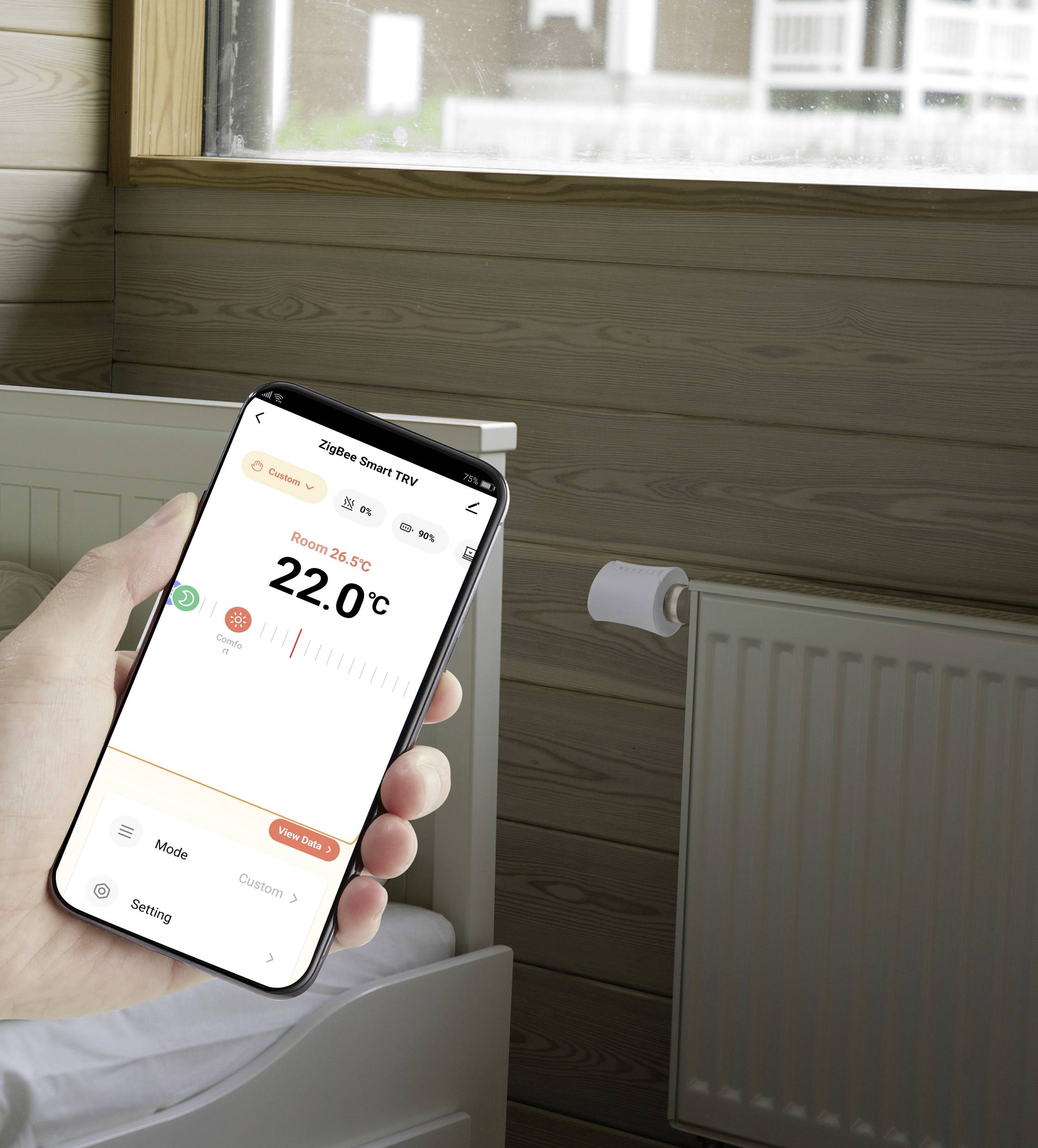 Een smartphone in de hand toont een app voor het regelen van de kamertemperatuur, die 22,0°C en de modus 'Aangepast' weergeeft. Op de achtergrond staat een verwarmingstoestel.