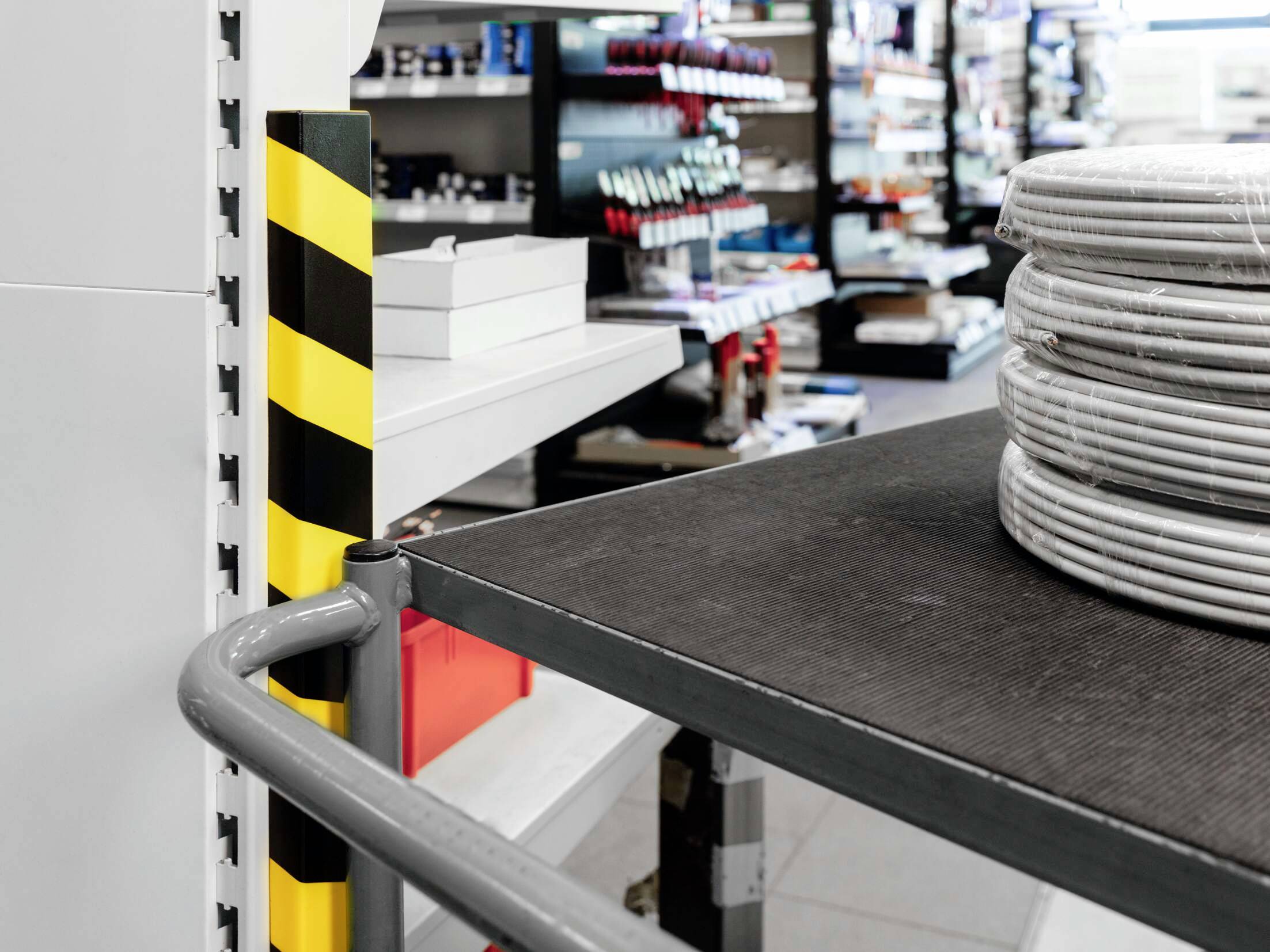 Stapel kabelrollen op een tafel in een magazijn, omringd door schappen vol producten van verschillende soorten.