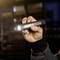 Een hand houdt een compacte LED-zaklamp vast die een fel lichtstraal uitzendt. Op de achtergrond is een onscherpe ruimte zichtbaar.