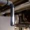 Een draagbare LED-zaklamp schijnt op een metalen leiding in een industriële omgeving. De zaklamp is aan de leiding bevestigd.