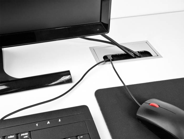 Monitor, toetsenbord en muis op een bureau, verbonden door kabels. De kabels lopen door een opening in het bureauoppervlak.