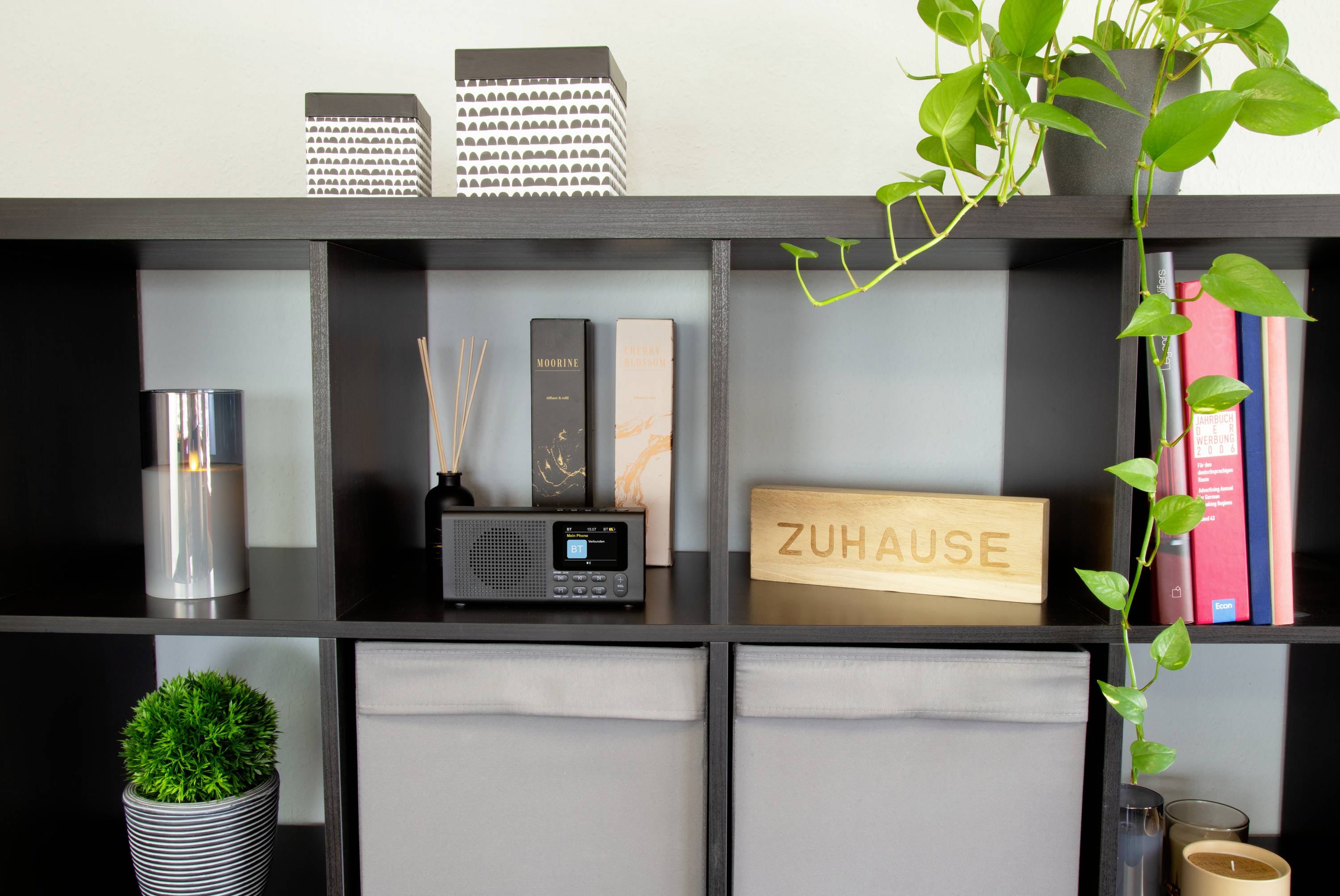 Een rek met decoratie-artikelen: boeken, een radio, planten en een bord met de tekst 'THUIS' voor een gezellige sfeer.