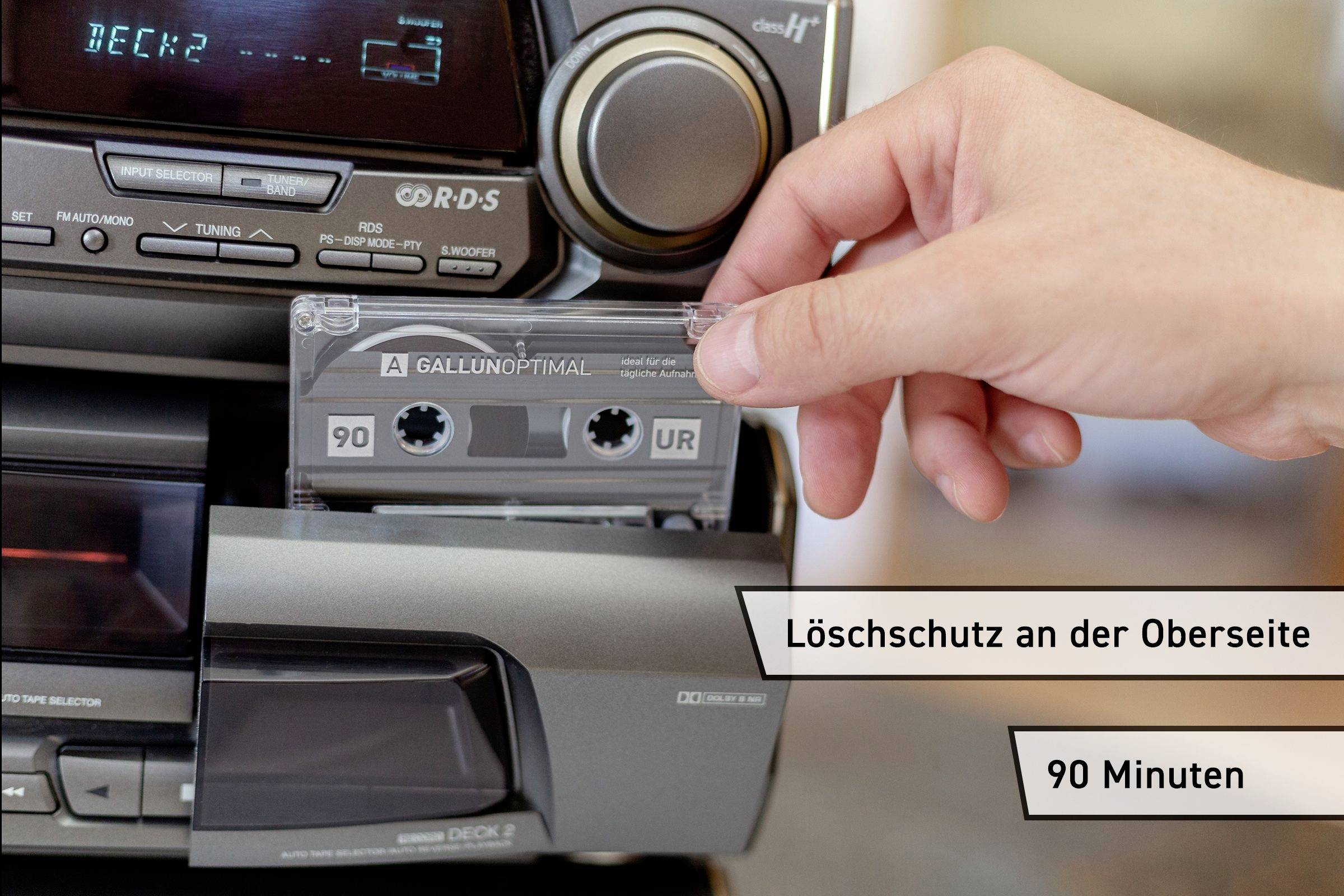 Een hand schuift een audiocassette in het cassettevak van een stereoapparaat. Opschrift: 'Verwijderbeveiliging aan de bovenkant', '90 minuten'.