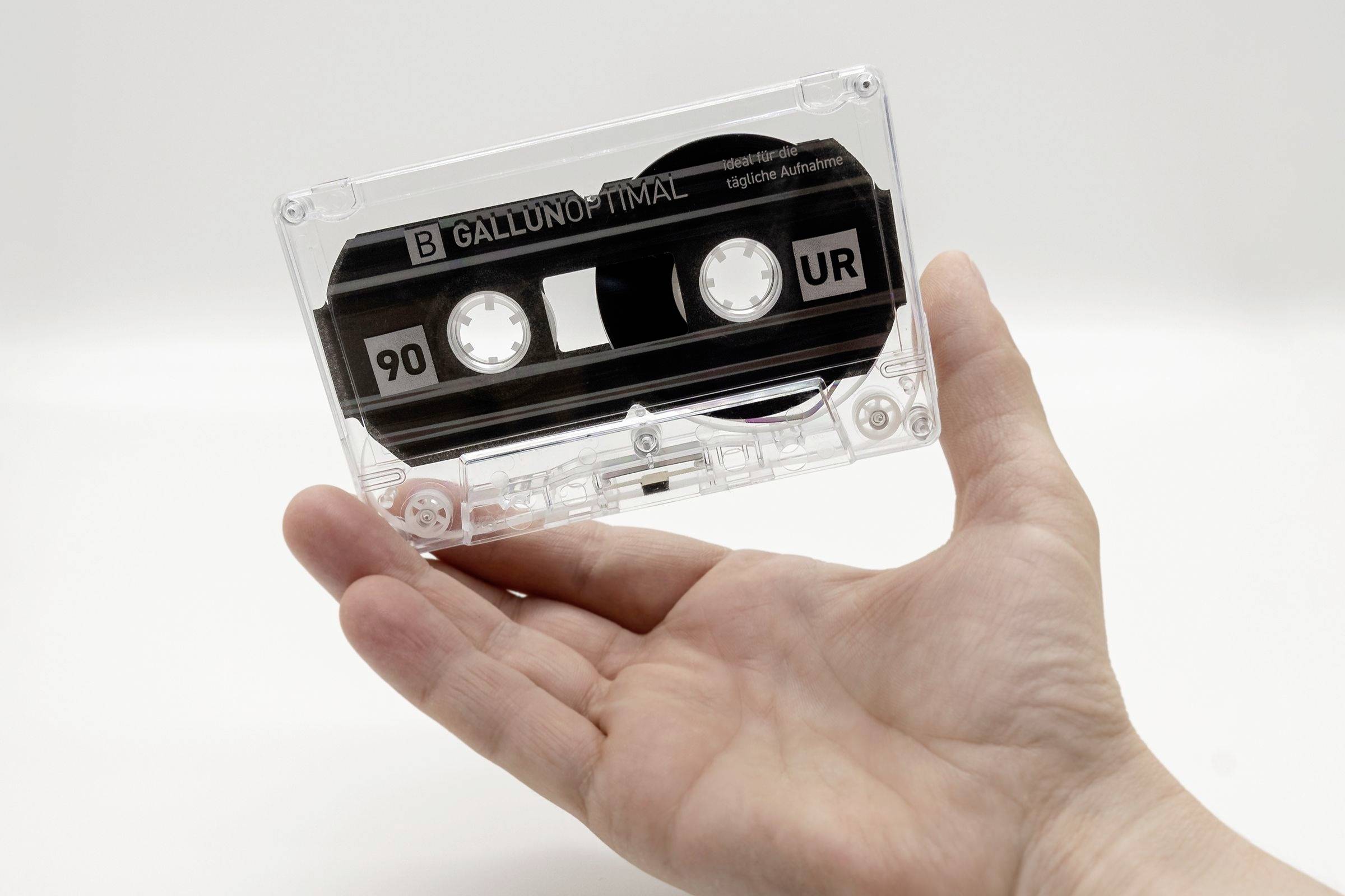 'Hand houdt een transparante audioband in de lucht, waarbij de opdruk '90 UR' en 'B GALLUJO' zichtbaar zijn.'