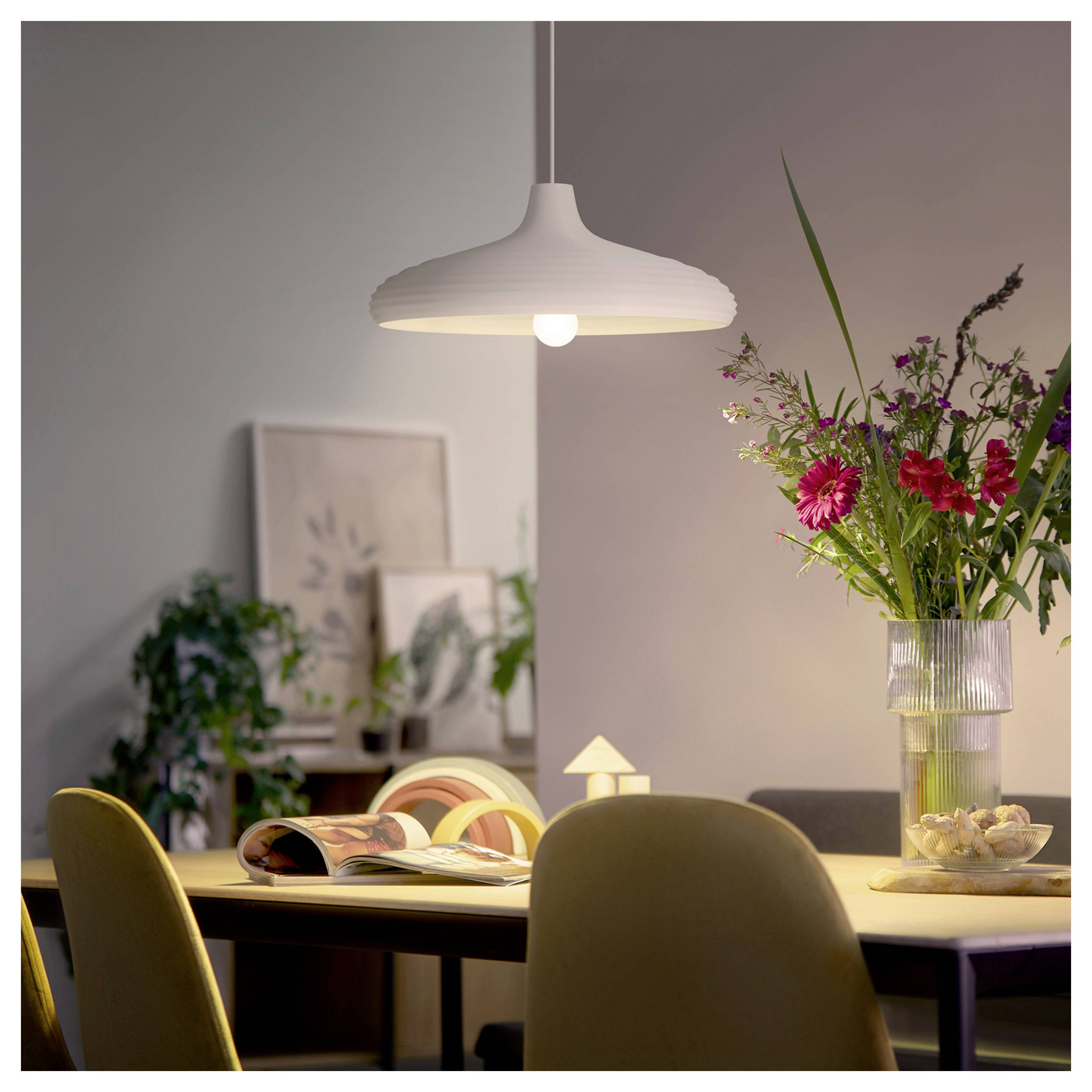 Modern eetkamer met een witte hanglamp boven een tafel met een opengeslagen boek en een vaas met bloemen.