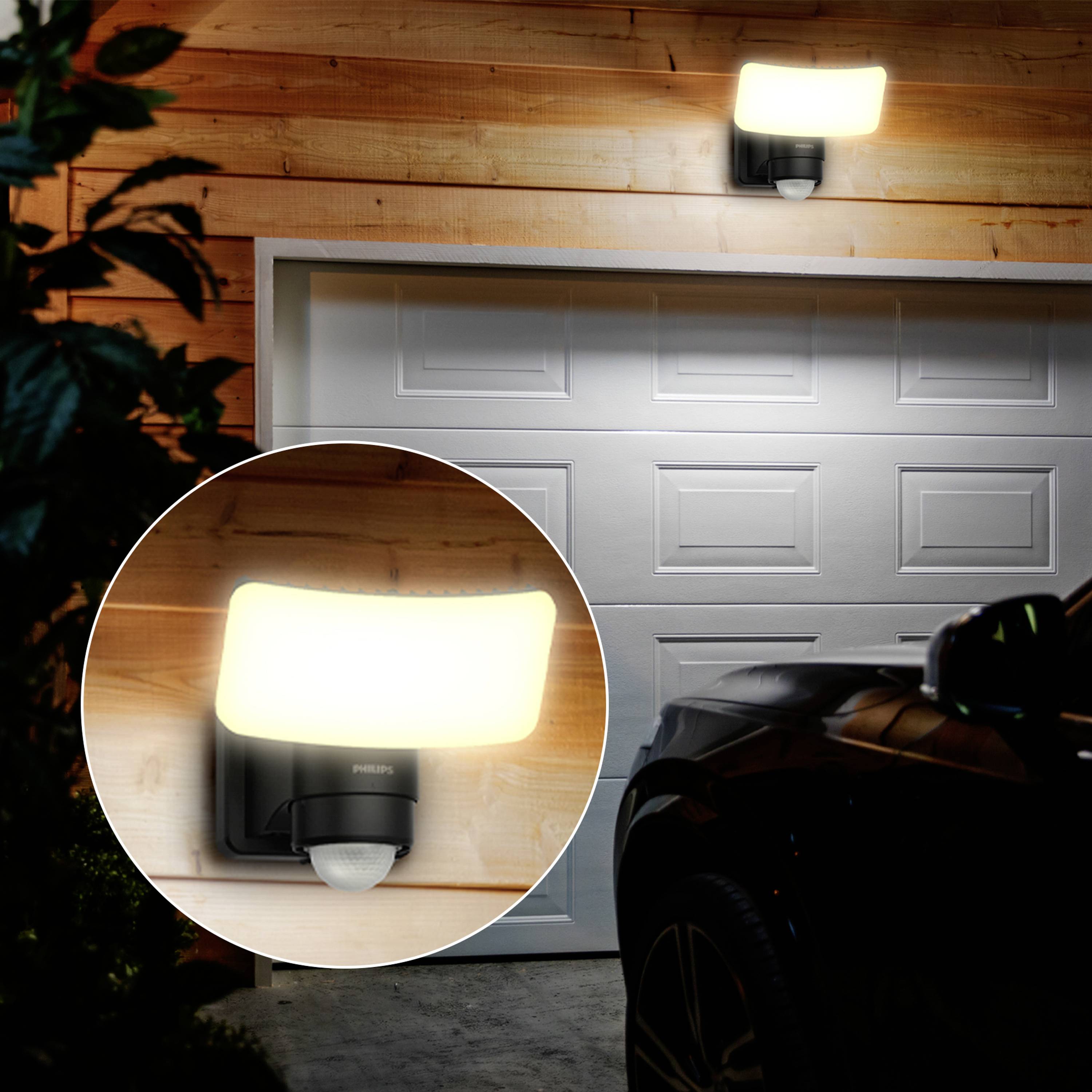 Een verlichte garagedeur met een nabije weergave van een sensorlamp die aan houten bekleding is bevestigd.