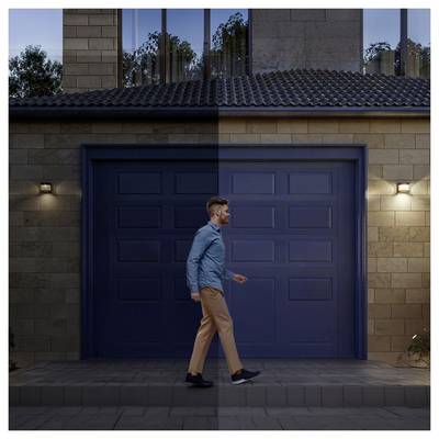 Man loopt langs een gesloten blauwe garagedeur in de schemering buiten een modern huis.