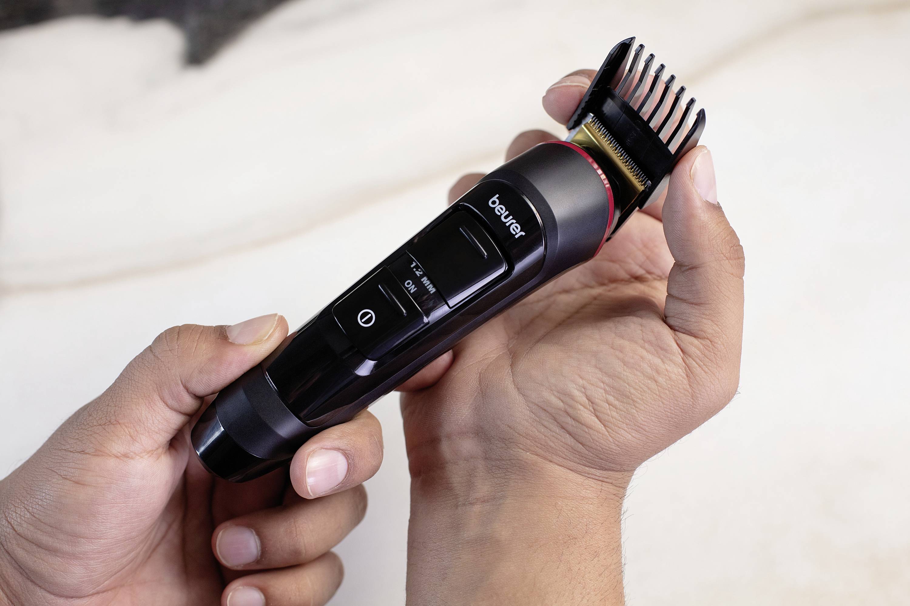 Een persoon houdt een elektrische haartrimmer met een zwart behuizing vast. De trimmer beschikt over een verstelbare opzetkam.