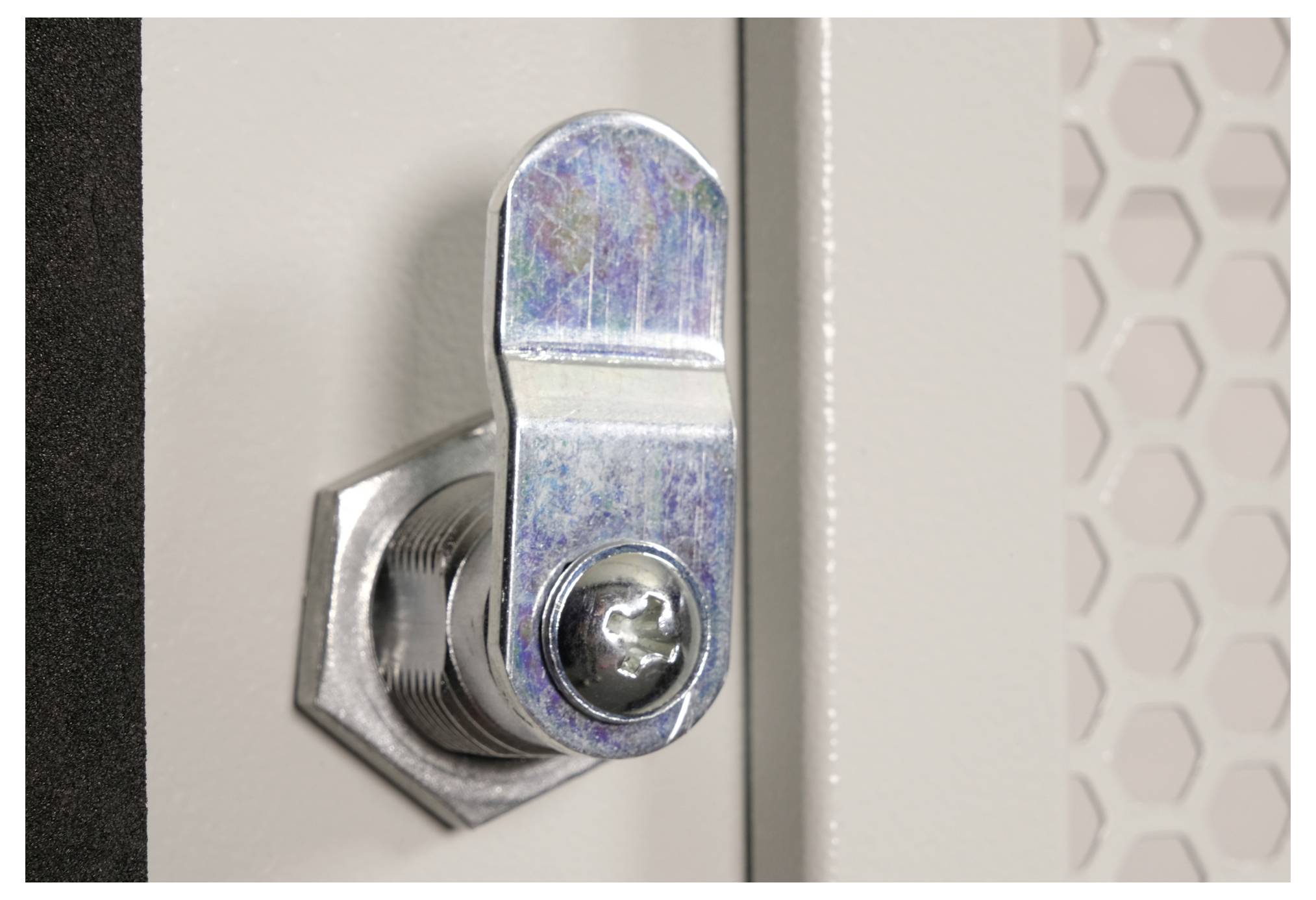 Close-up van een metalen vergrendelingsmechanisme bevestigd aan een lichtgekleurde oppervlakte, met een gestructureerd rasterpatroon zichtbaar op de achtergrond.