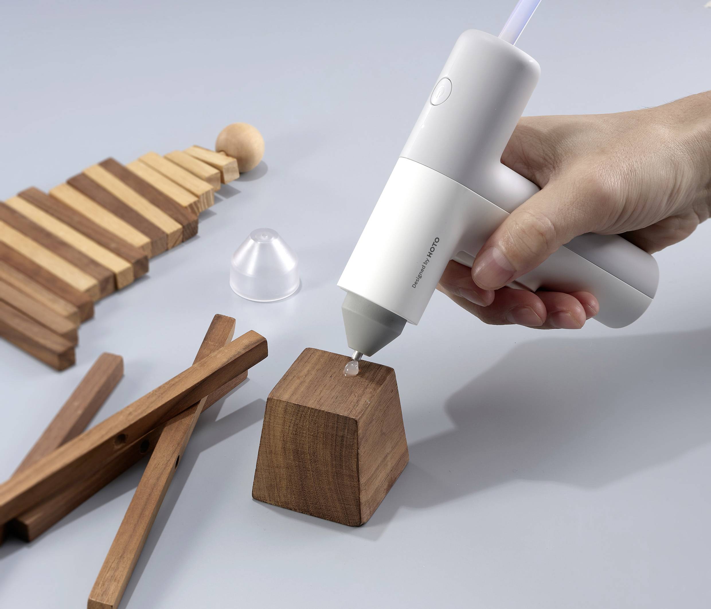 Een hand gebruikt een lijmpistool om een houten blok te lijmen. Ernaast liggen houten onderdelen die blijkbaar moeten worden gemonteerd.