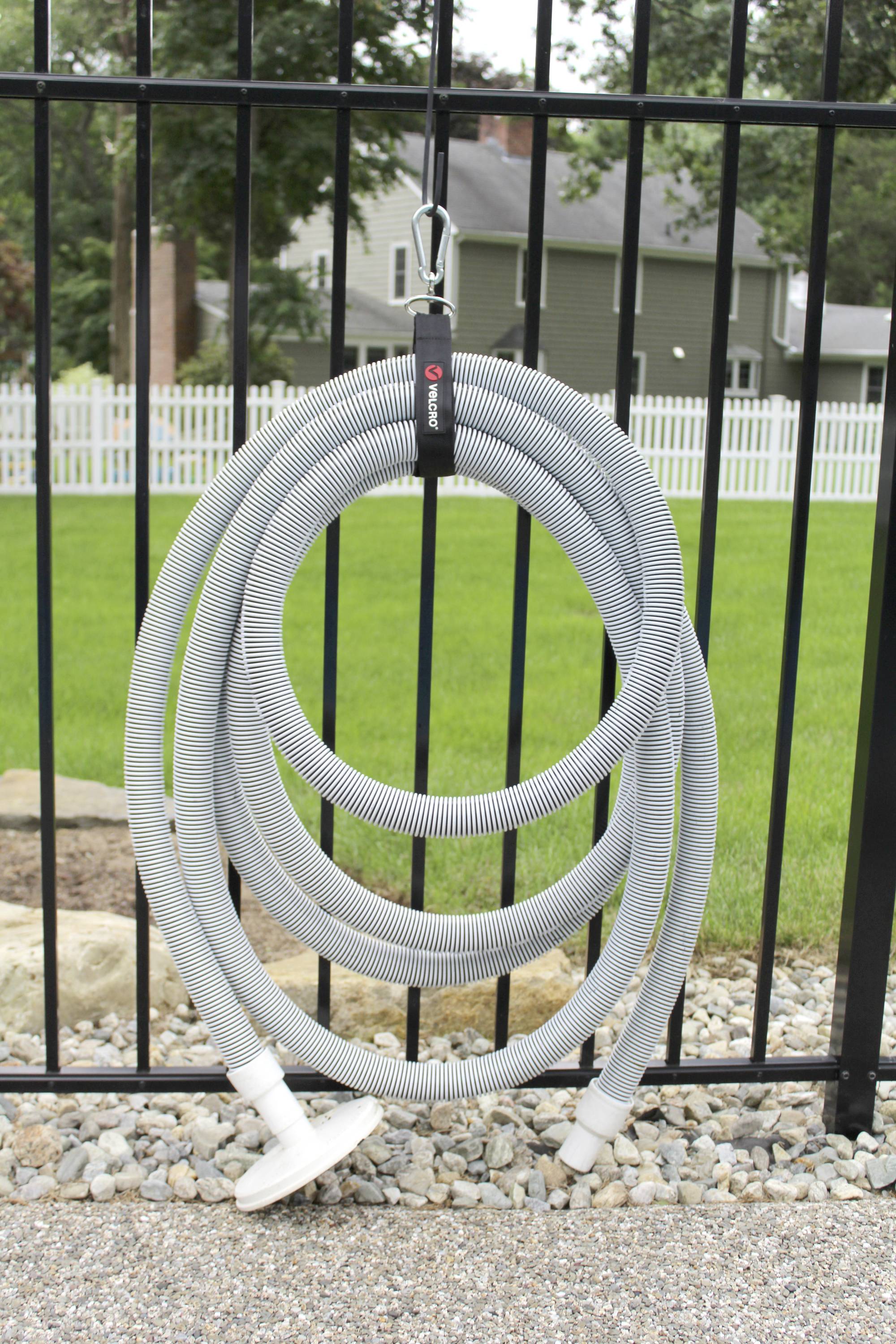 Grijze zuigslang hangt aan een zwart metalen hek; op de achtergrond een groene tuin en een wit houten hek.