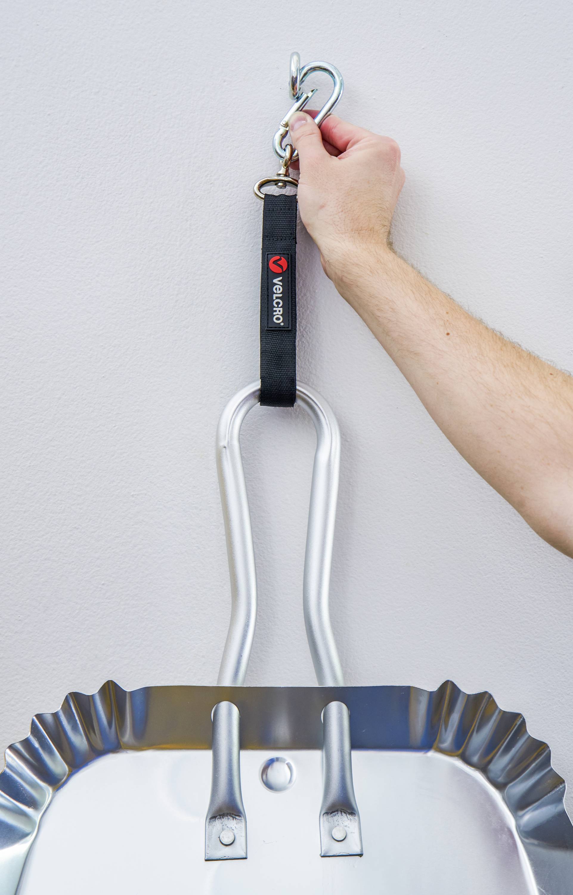 Een hand hangt een sneeuwschep aan de muur met een zwarte haak.