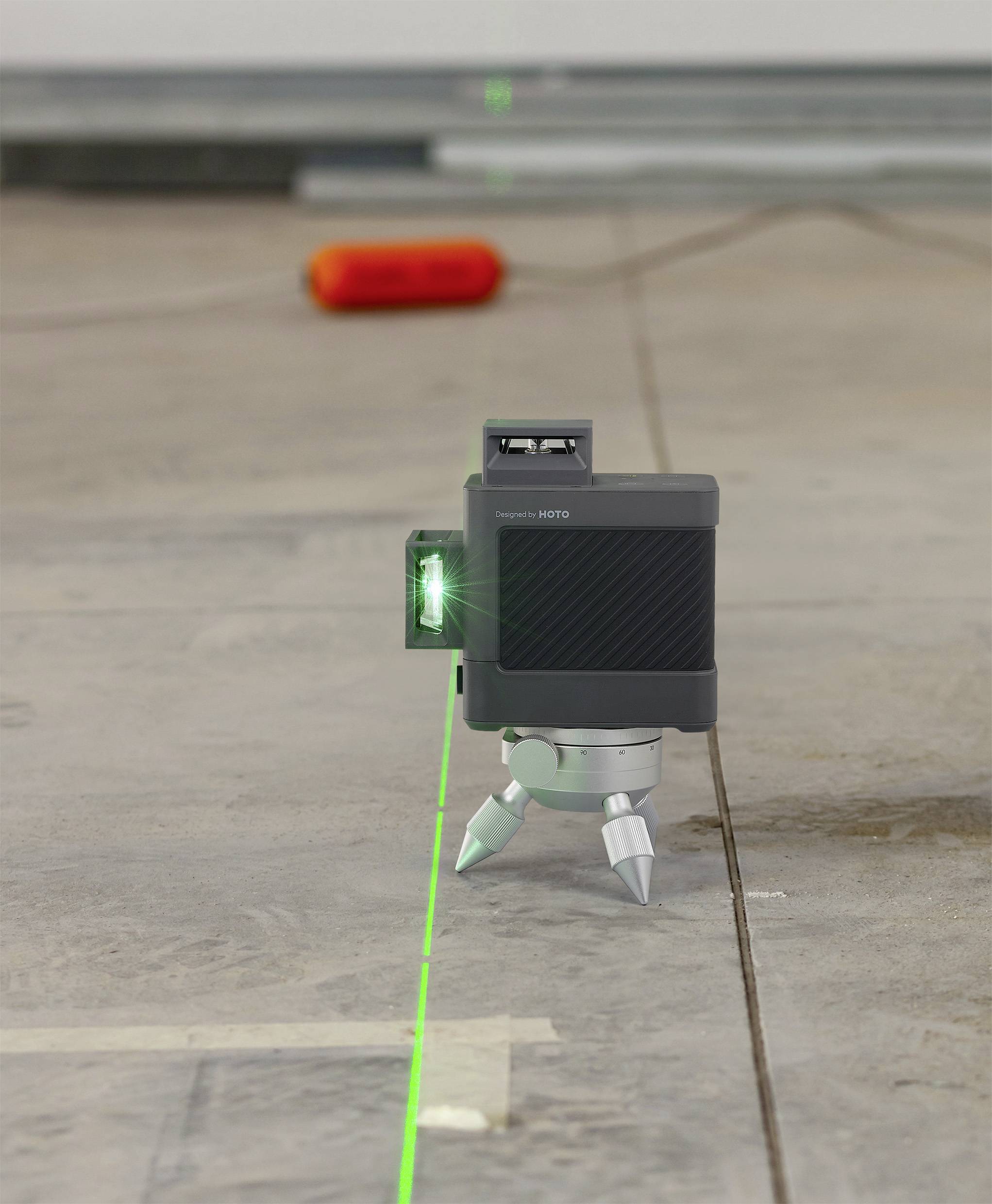 Een lasermeetapparaat projecteert een groene lijn op de vloer om een rechte uitlijning te garanderen. Op de achtergrond ligt een rood apparaat.