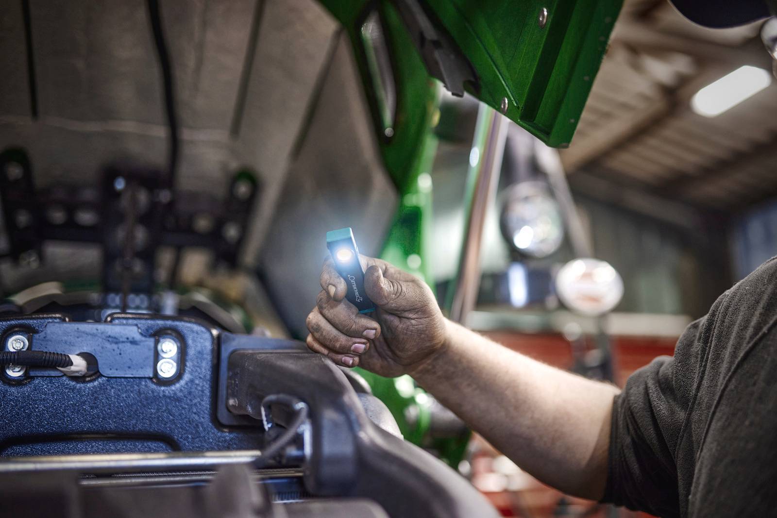 Een persoon inspecteert de motorruimte van een voertuig met een zaklamp om mechanische problemen te identificeren.