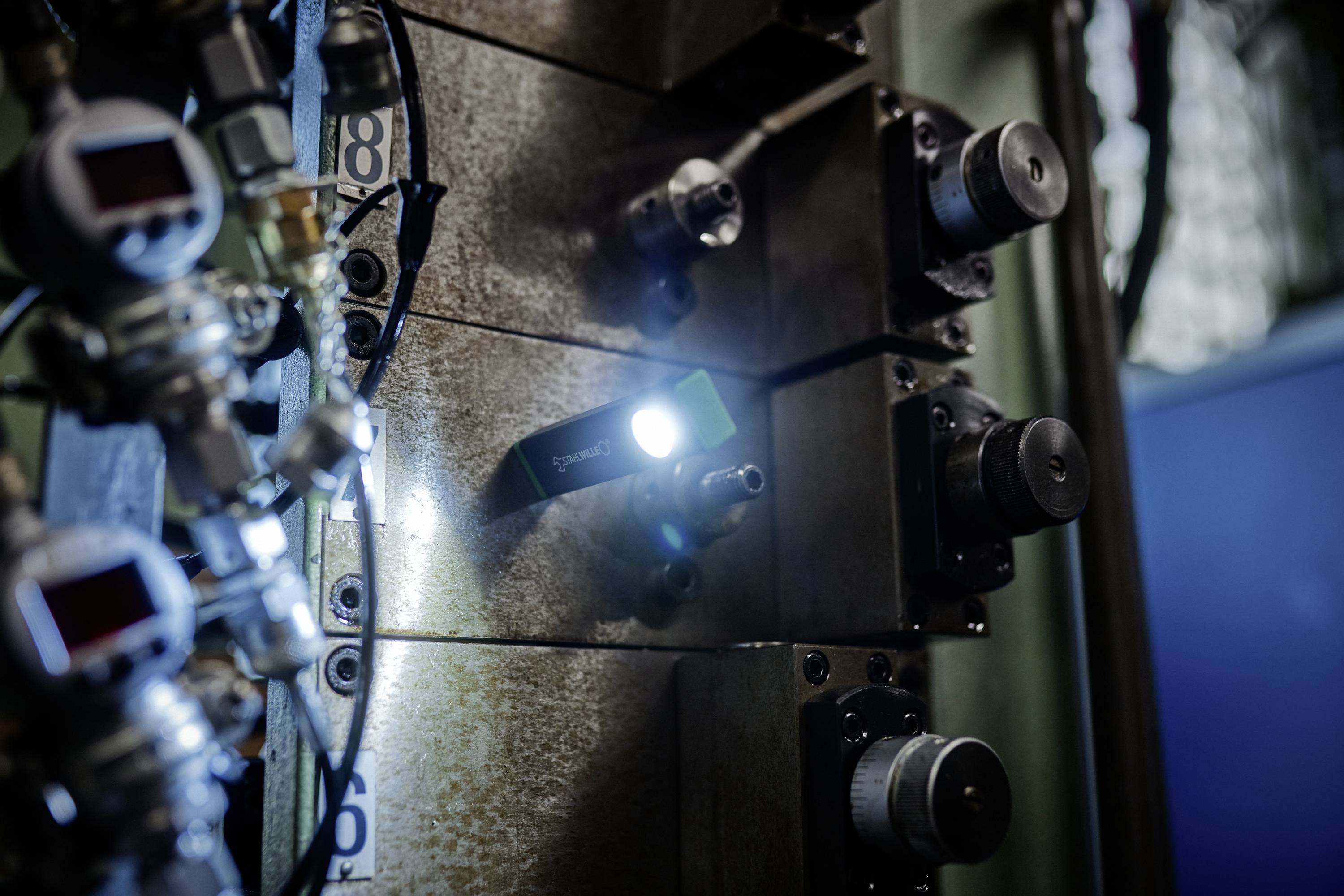 Een close-up van industriële machinerie met meerdere tandwielen en knoppen. Een klein licht verlicht een deel van de apparatuur, waardoor schaduwrijke gebieden ontstaan.